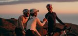 Drei Personen stehen mit Rennrädern im Abendlicht auf einem Hügel und zwei geben sich die Hand.