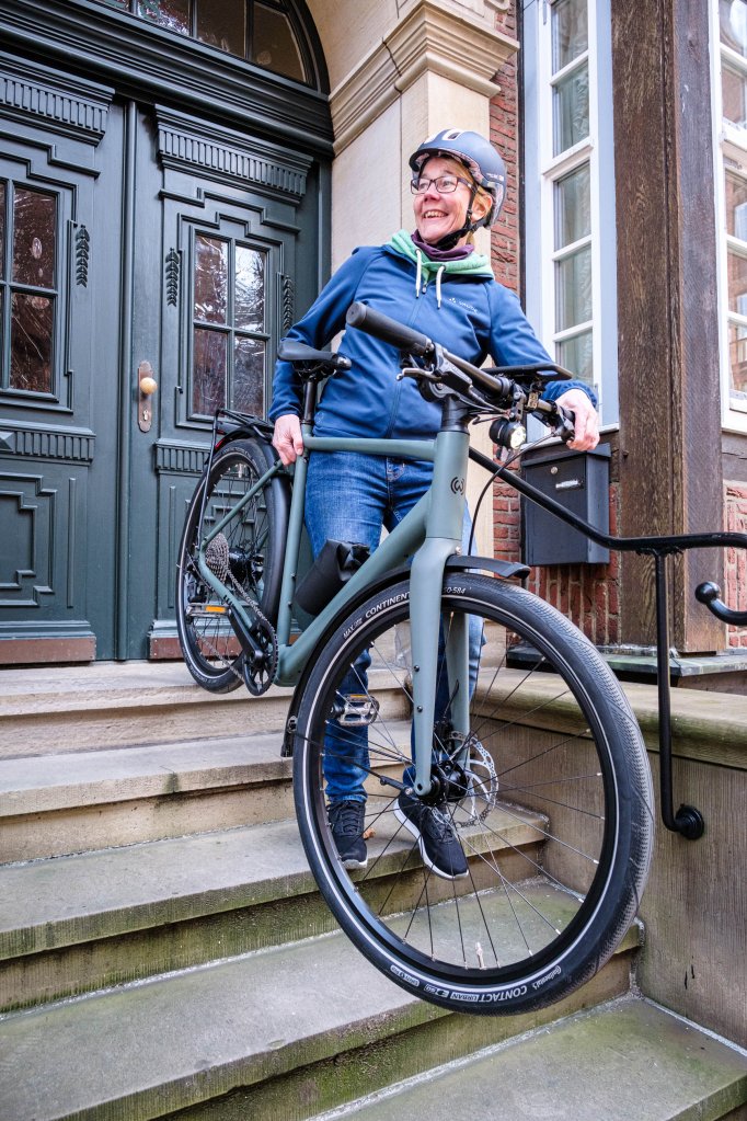 Eine Frau trägt ein Fahrrad die Treppe vor einer Haustür hinab.