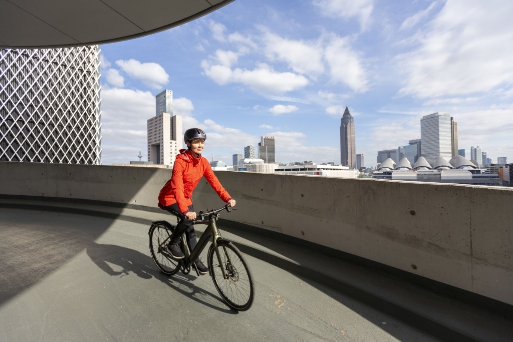 Eine Frau fährt mit einem E-Bike vor der Skyline von Frankfurt entlang.