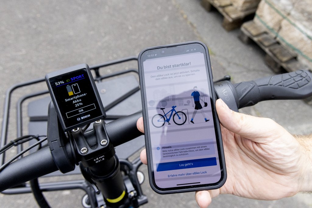 Hand hält Smartphone an E-Bike-Display.