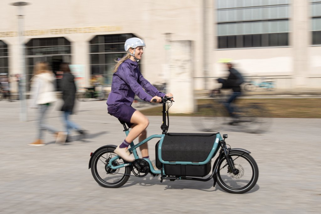 Frau fährt mit E-Lastenrad durch Stadt.