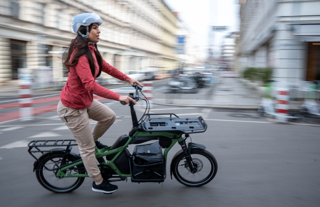 Frau fährt mit einem Lastenrad durch die Stadt.