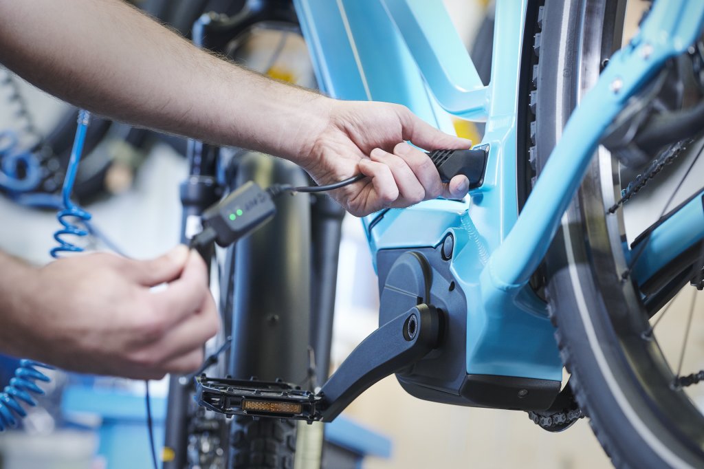 Die Hände einer Person, die ein Ladekabel am Rahmen eines E-Bikes anschließt oder abzieht.